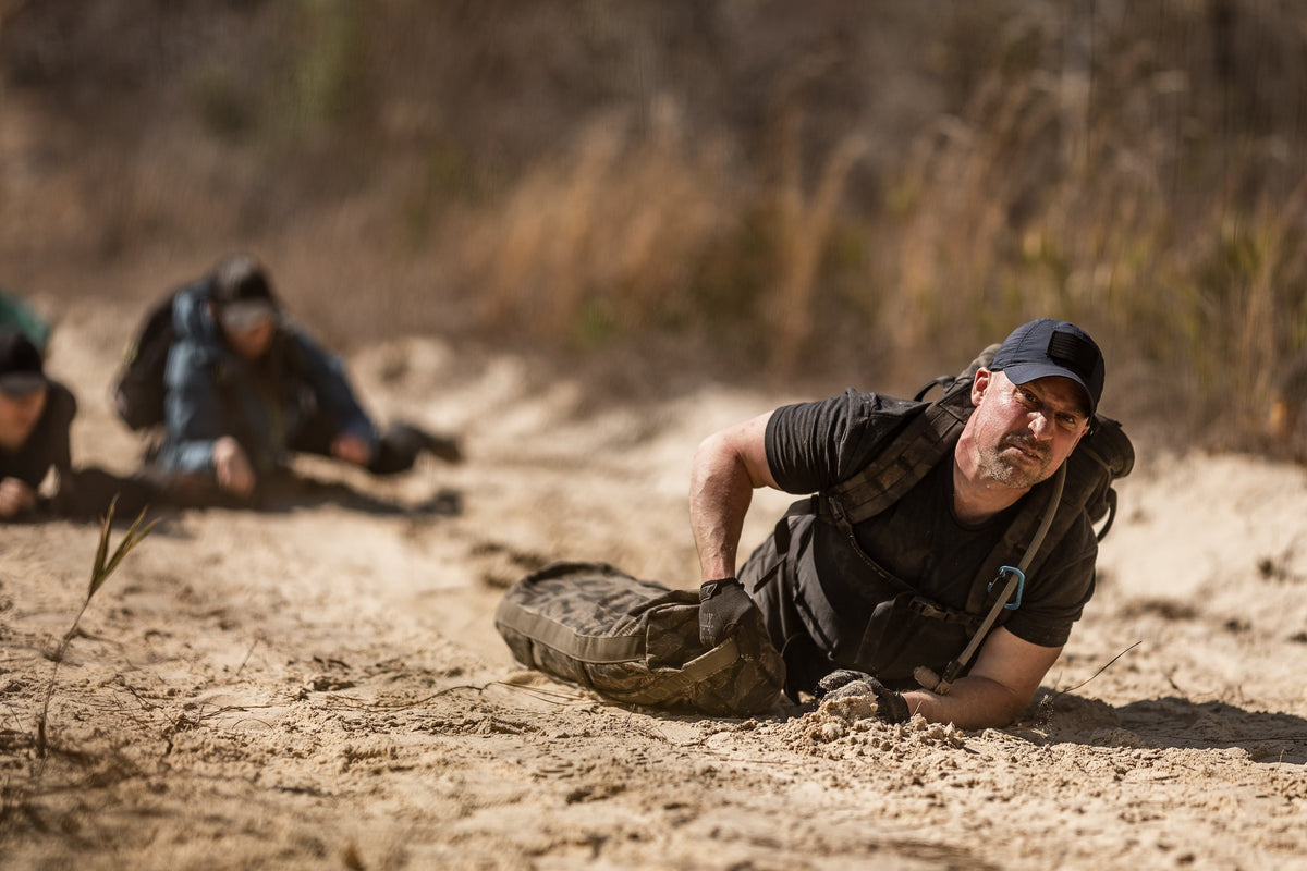 Man wearing GORUCK rucking gear crawling in sand during outdoor endurance training
