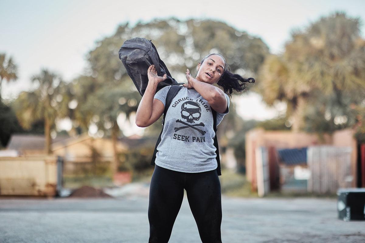 Woman training outdoors with GORUCK sandbag, wearing GORUCK Tribe Seek Pain shirt