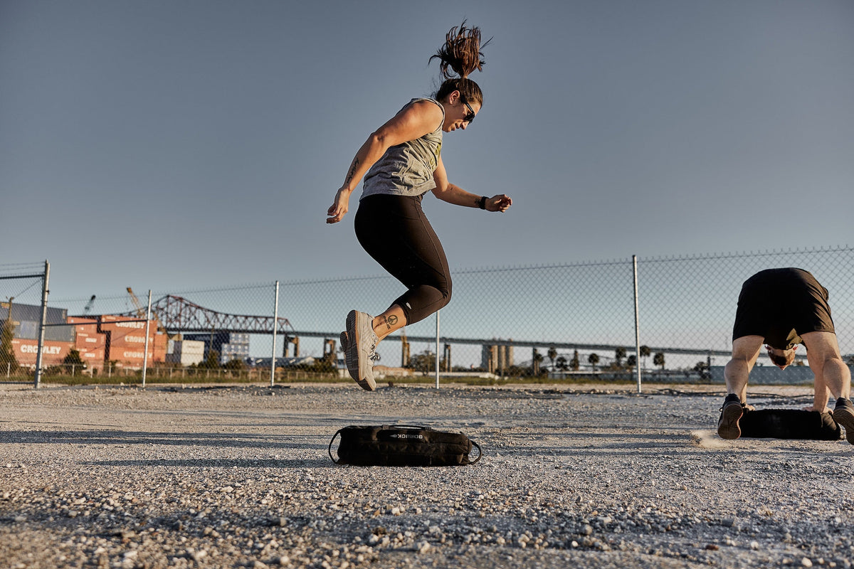 Woman jumping over a GORUCK sandbag outdoors during rucking workout