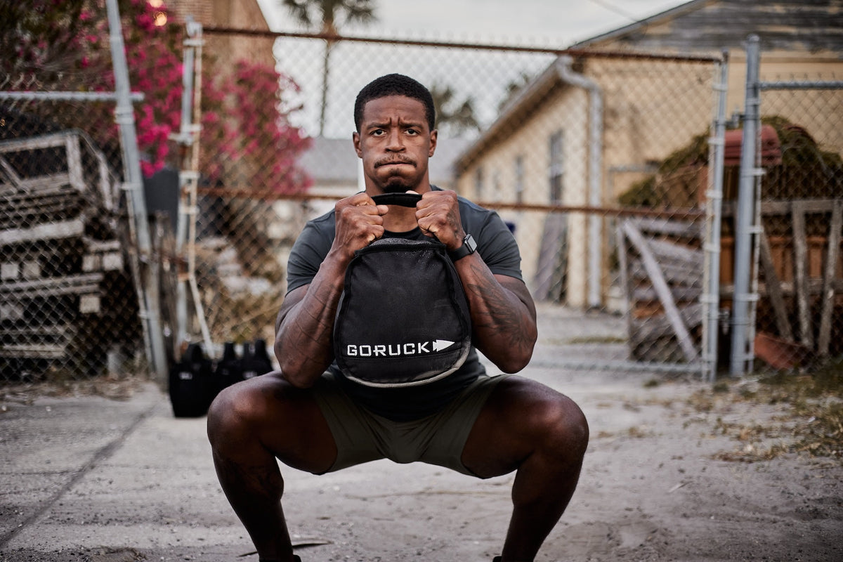 Man outdoors performing squat with GORUCK sandbag, showcasing durable rucking gear.