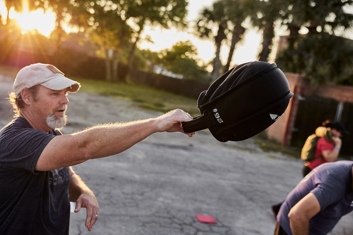 Man exercising outdoors with GORUCK 26-pound ruck sandbag at sunrise, outdoor fitness training