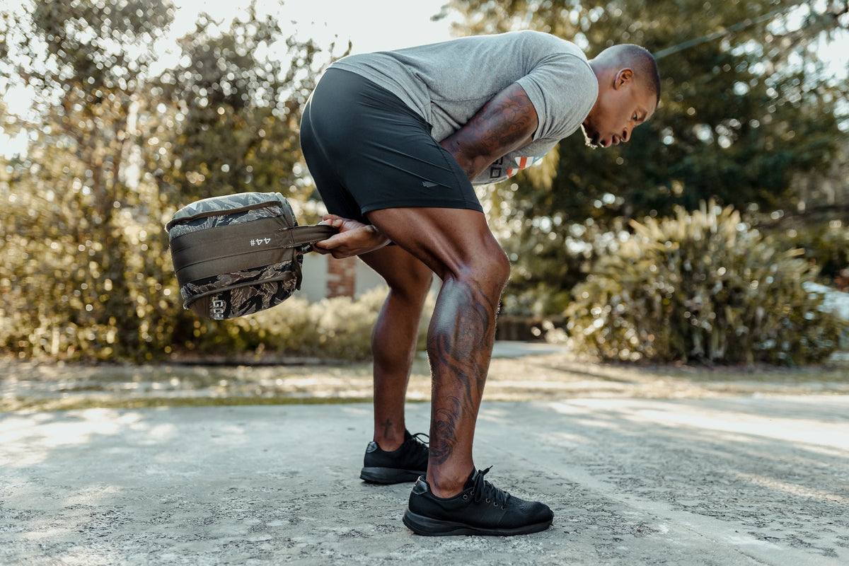 Man outdoors performing rucking exercise with GORUCK weighted sandbag, wearing athletic gear.