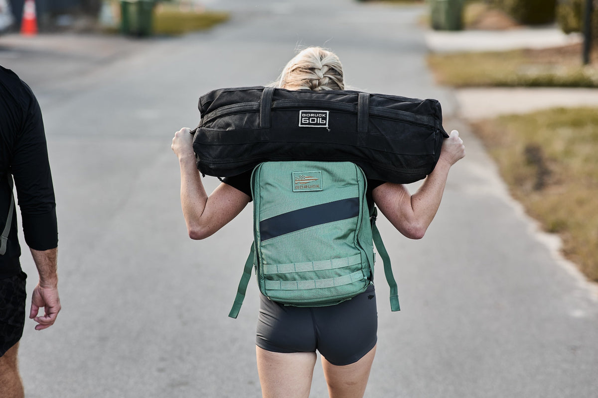 Person rucking with a GORUCK backpack and sandbag on a suburban street