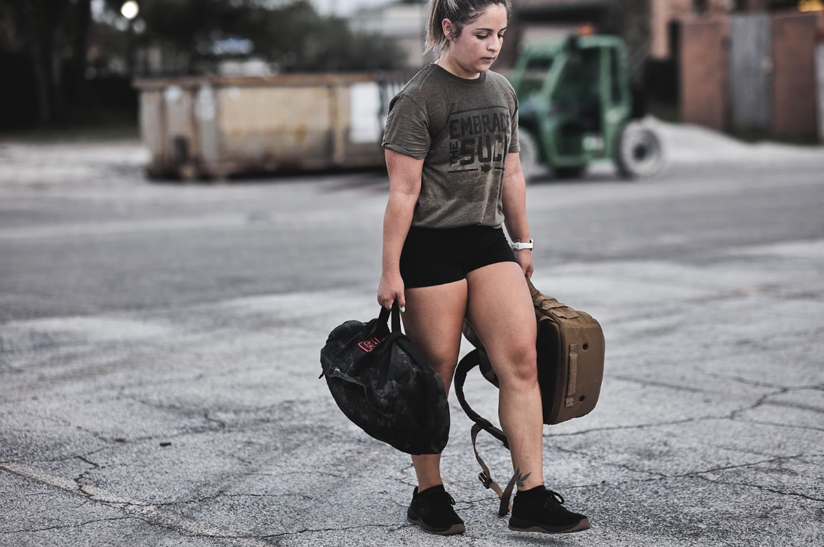 Woman rucking outdoors with GORUCK gear, carrying weighted backpack and sandbag, fitness training