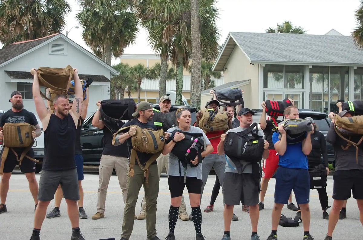 Group of people outdoors lifting GORUCK rucksacks during a rucking fitness event