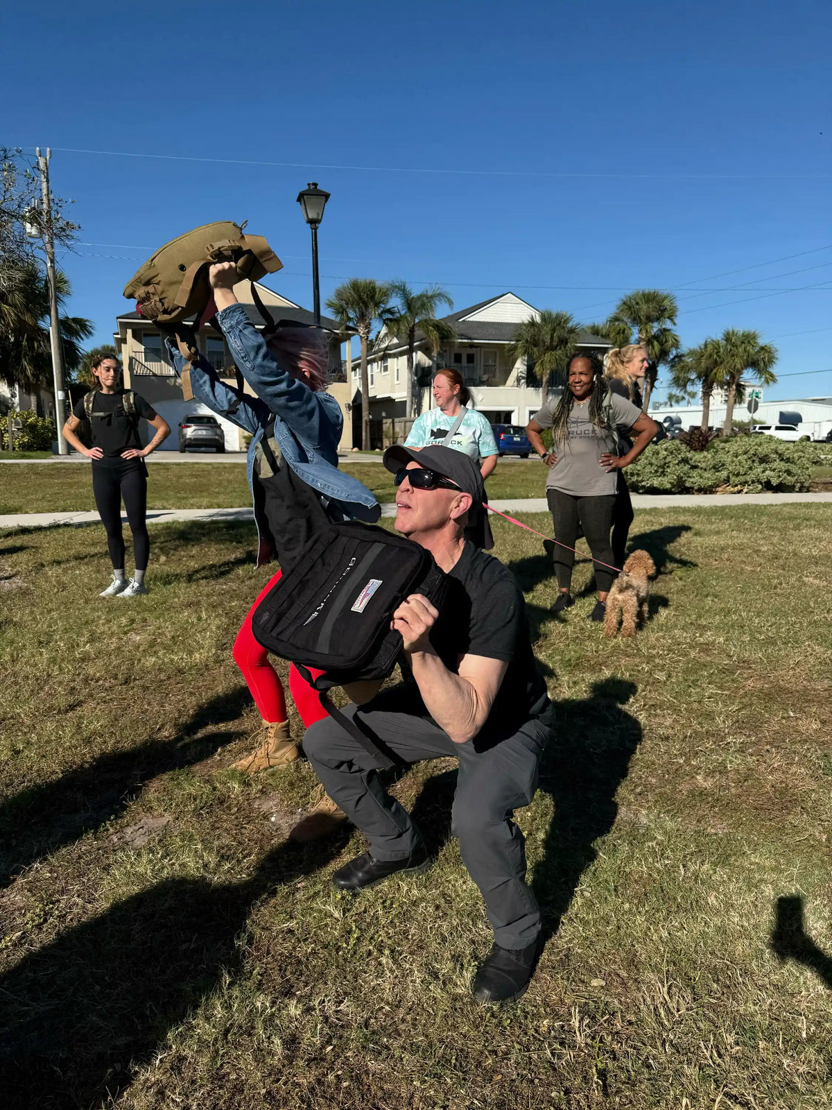 Group outdoor rucking workout with GORUCK gear, people exercising on grass under blue sky