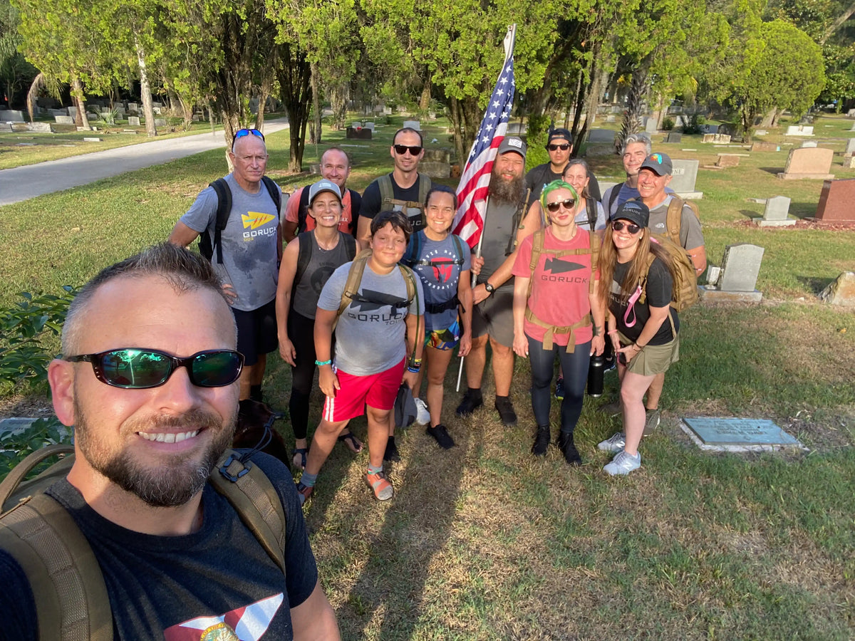 GORUCK group rucking with backpacks and American flag in a cemetery, outdoor training event