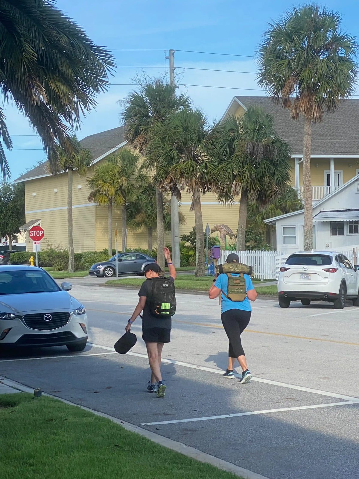 Two people with GORUCK rucksacks rucking on a sunny street lined with palm trees