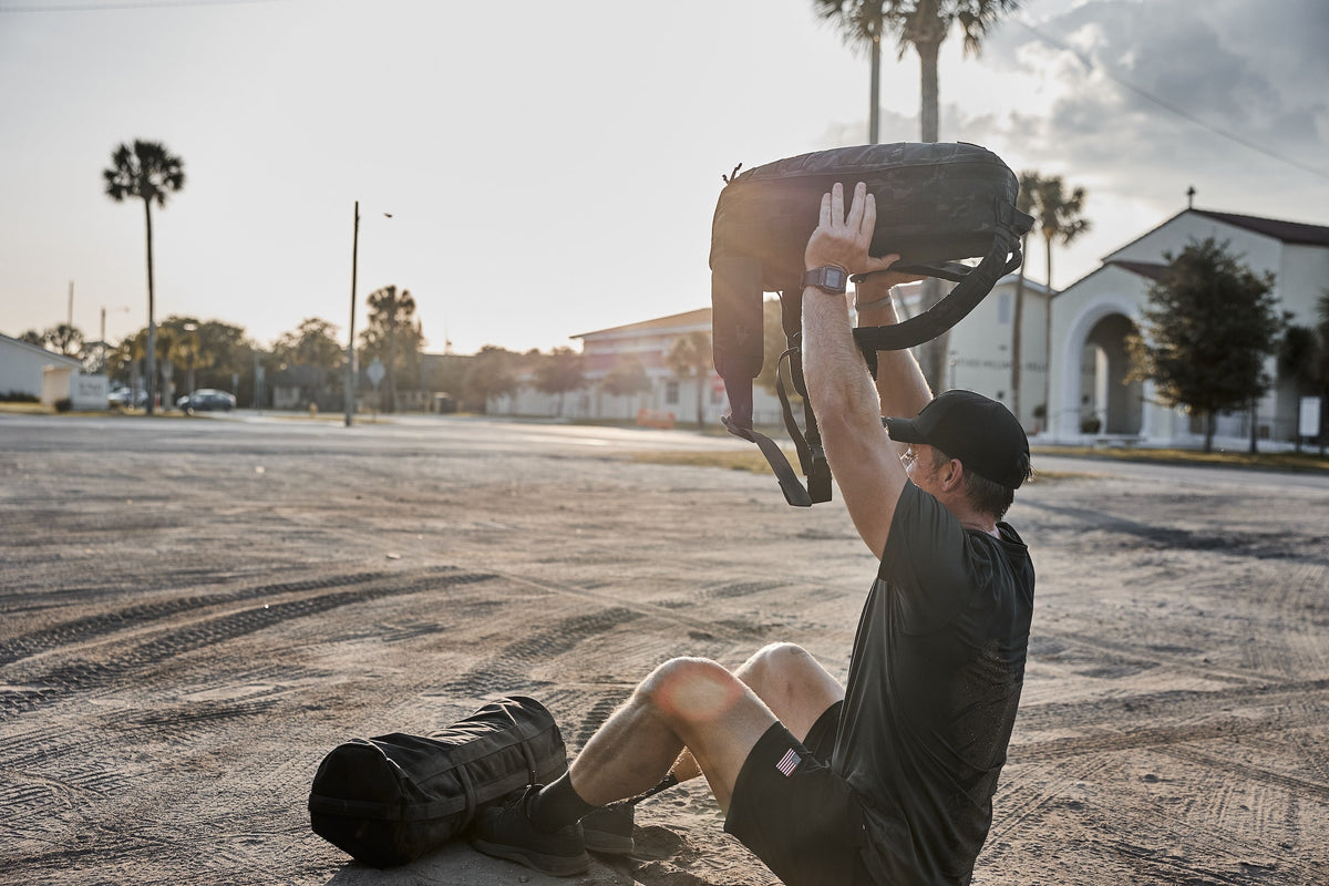 Man doing outdoor rucking workout with GORUCK backpack and sandbag at sunrise
