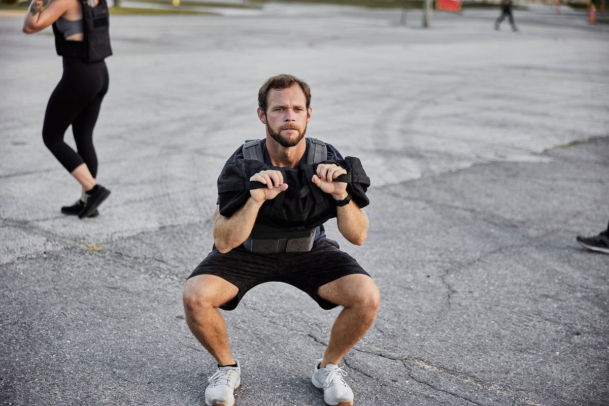 Man performing outdoor squat wearing a ruck plate carrier, GORUCK fitness training gear