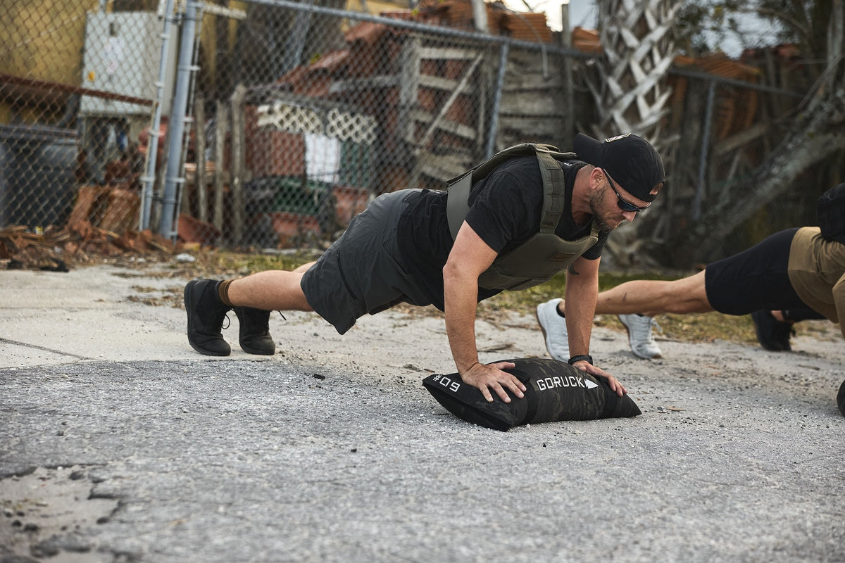 Man in tactical vest doing outdoor push-ups with GORUCK sandbag, fitness rucking gear