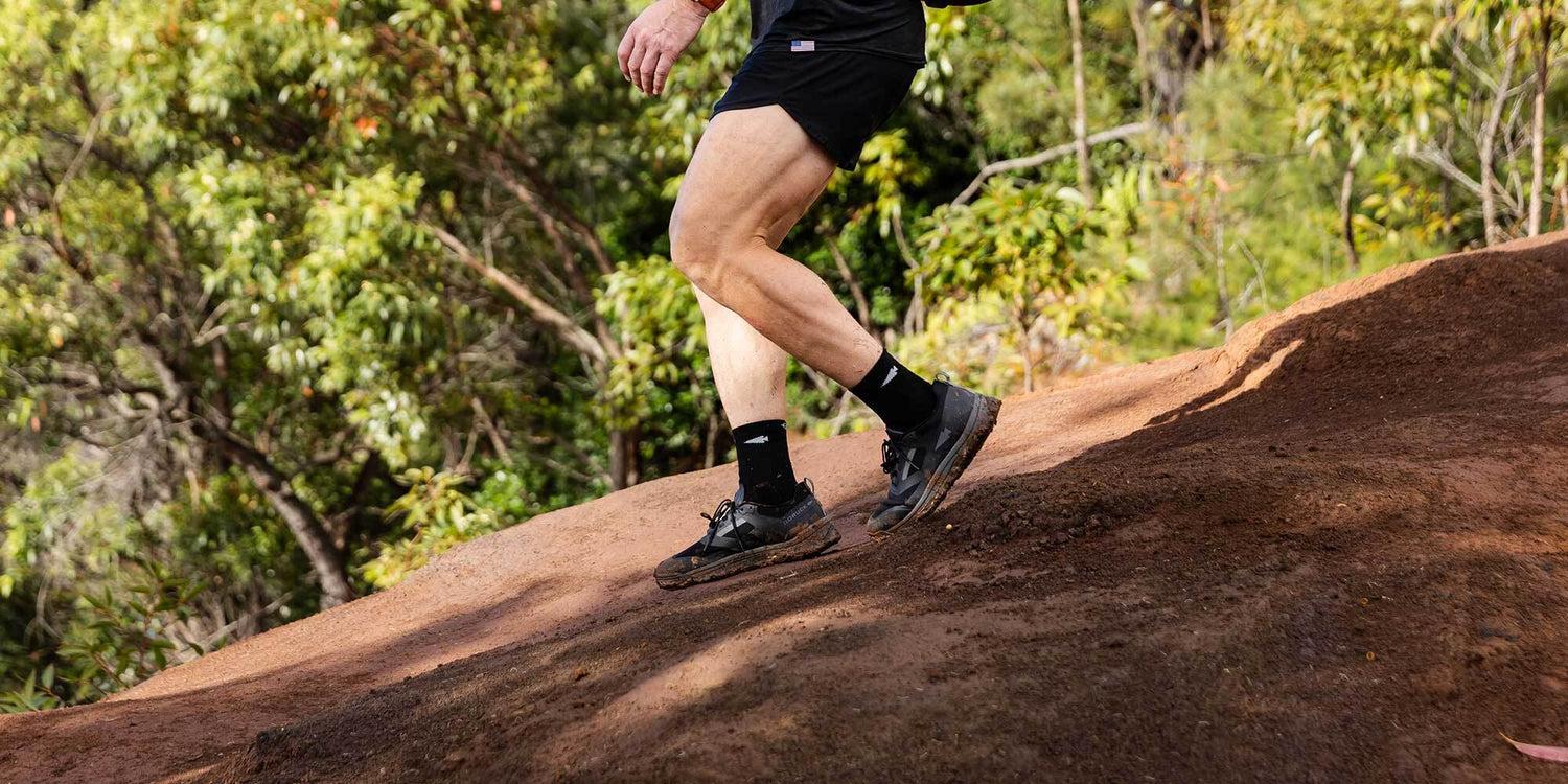 Person trail running on a sloped path surrounded by trees.