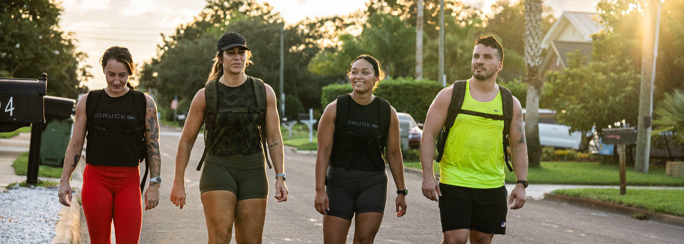 Four people in athletic gear walking on a sunny street with trees and houses in the background.