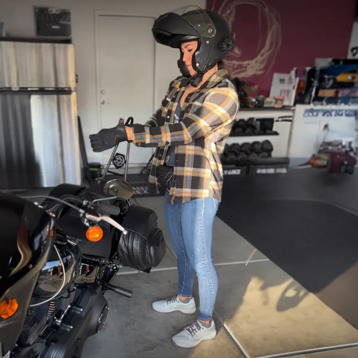 A person in a helmet and gloves stands by a motorcycle in a garage, preparing to ride.