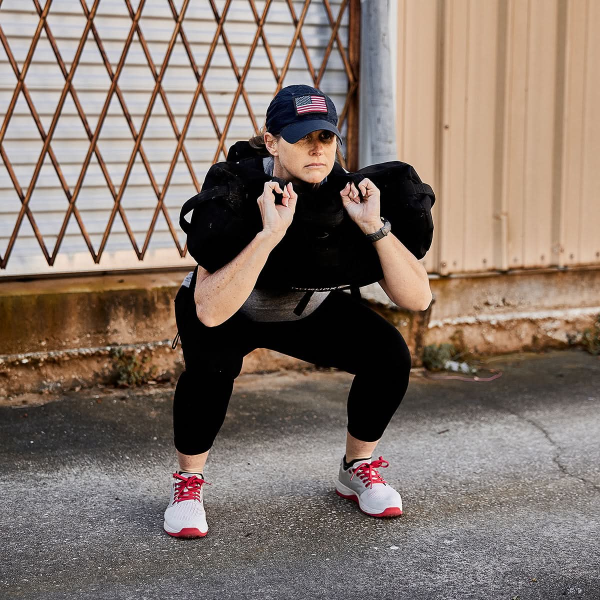 Someone is squatting outdoors with a weighted bag on their shoulders, wearing athletic gear and a cap, demonstrating the art of rucking with the Ruck Clubs Starter Kit - Light by GORUCK.