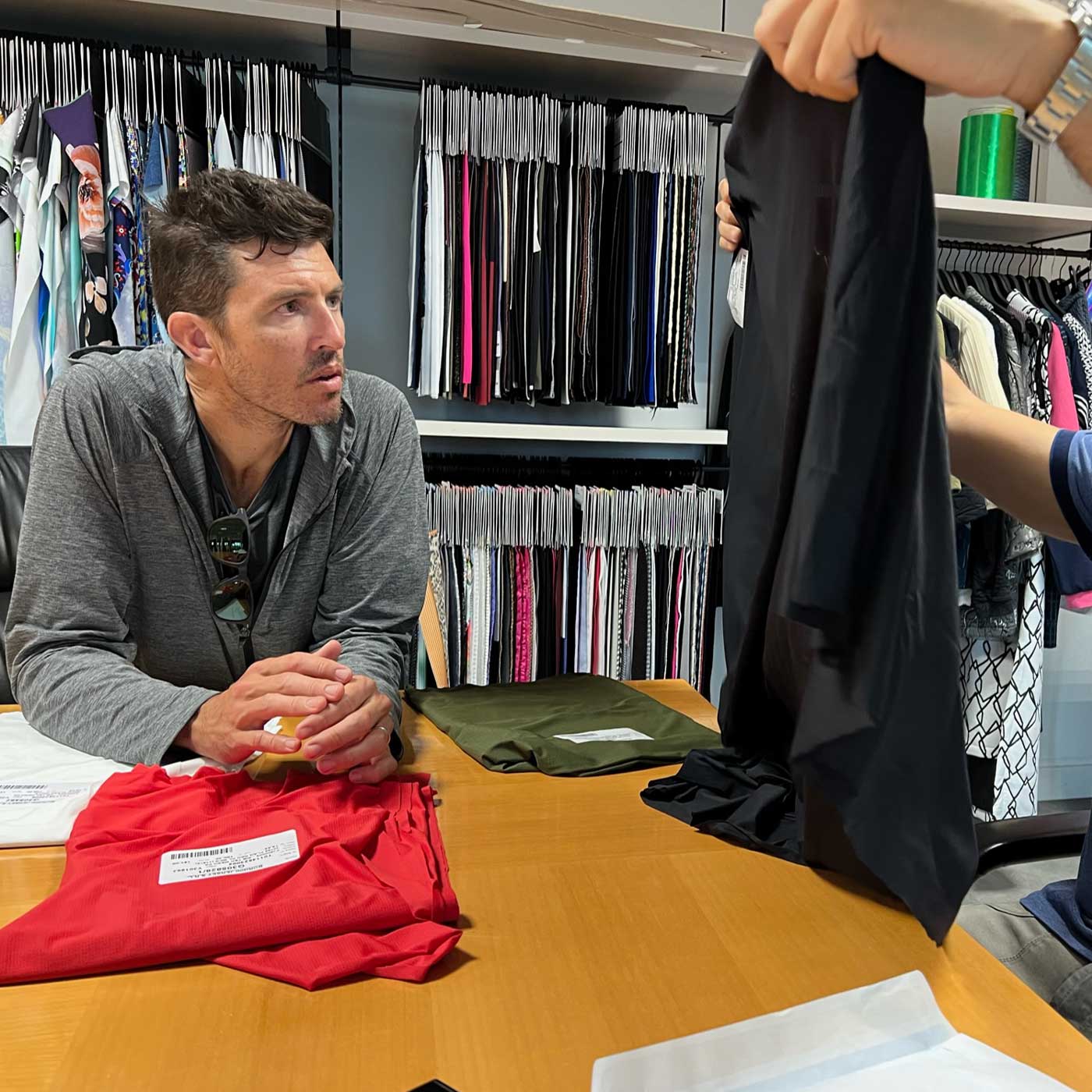 A man examines fabric samples at a table, with shelves of fabric rolls in the background.