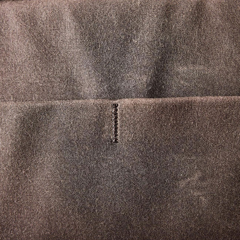 Close-up of brown fabric with a horizontal seam and a small vertical row of black stitches in the center.