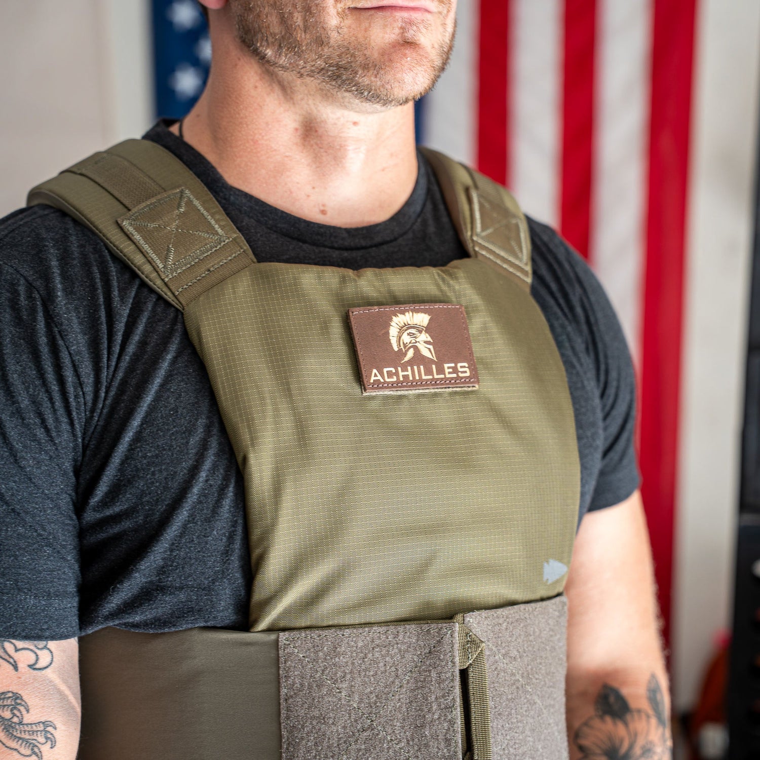 A man, visible from chest up, wears the Achilles Vest in front of an American flag.