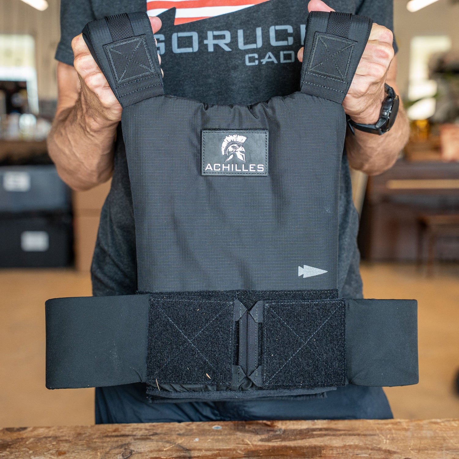 Person holding a black Achilles | Men's Weighted Vest featuring thick straps and a Velcro waistband, designed for safe and effective premium training.
