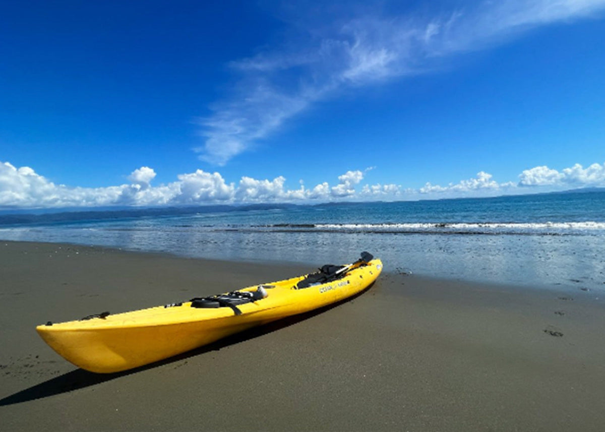 A yellow kayak rests on a sandy beach with gentle waves and a bright blue sky with clouds.