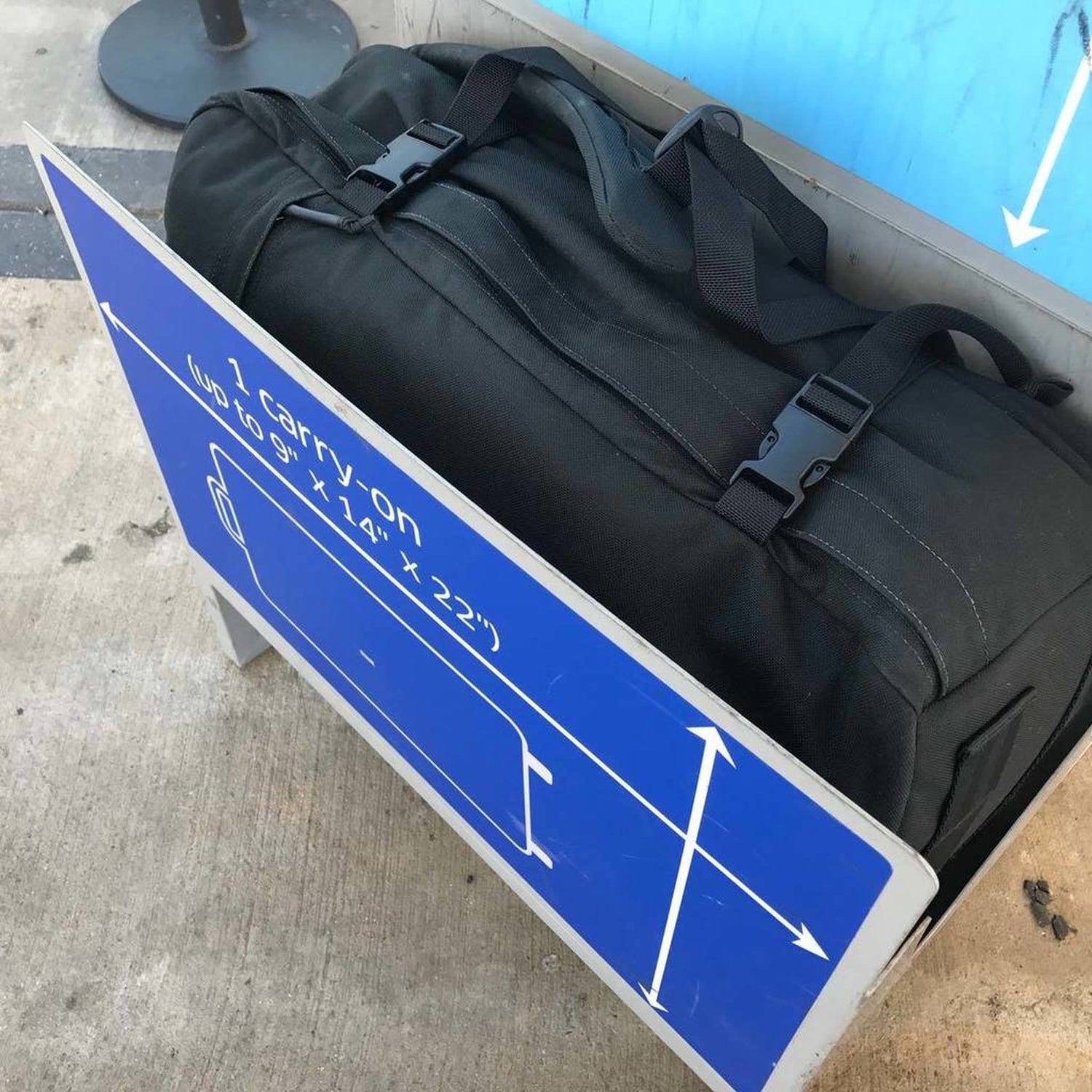 A black duffel bag placed inside a carry-on luggage sizer at an airport.