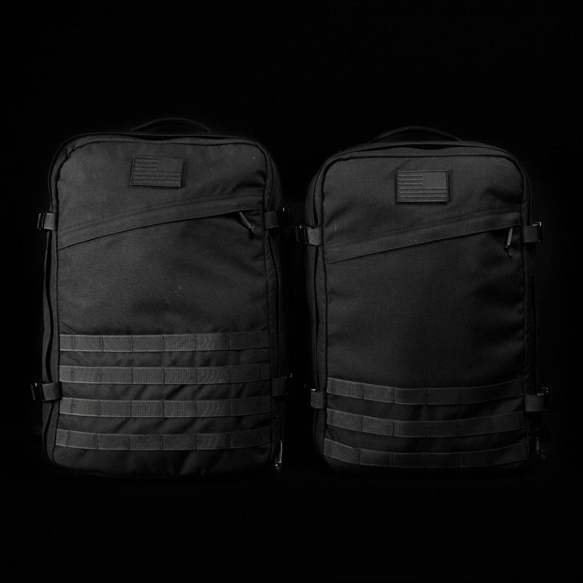 Two black tactical backpacks with horizontal webbing sit side by side against a black background.