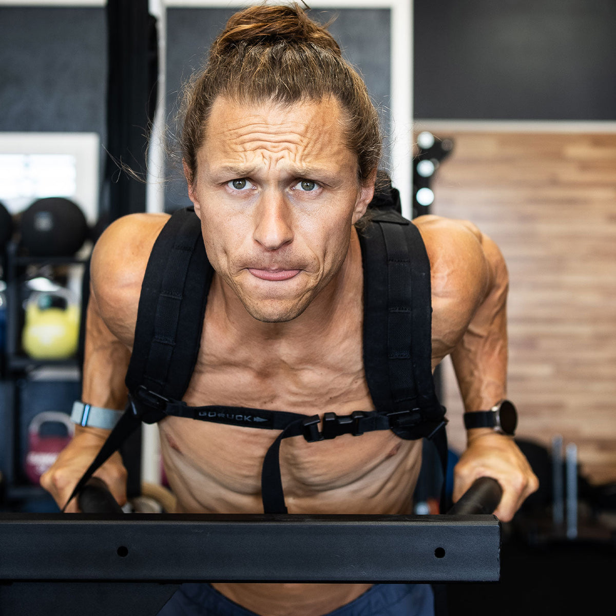 Man with a topknot using parallel bars for weighted dips in a gym, looking focused and intense.