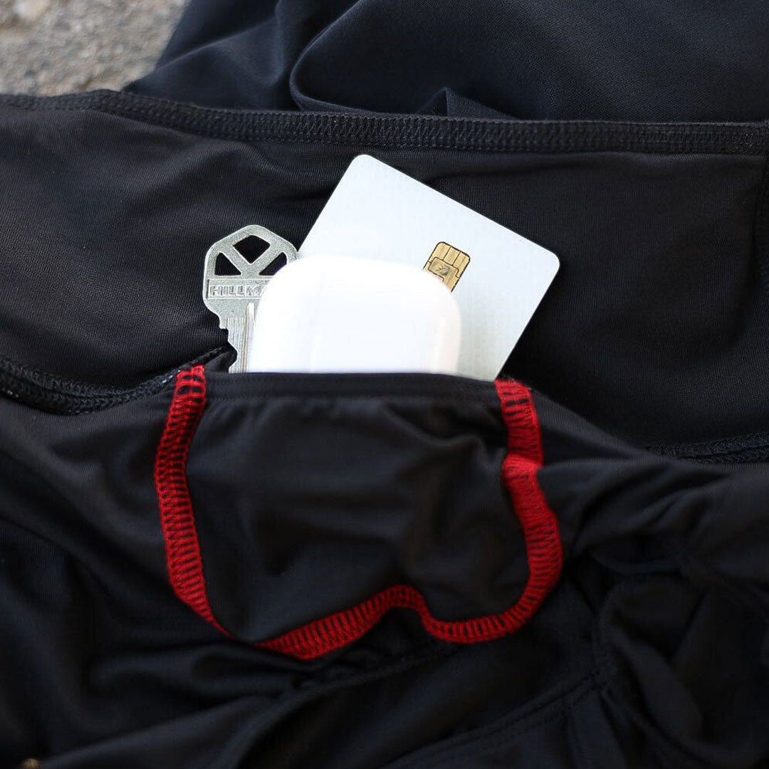 A small pocket in black athletic clothing holds a key, a card, and white wireless earbuds.