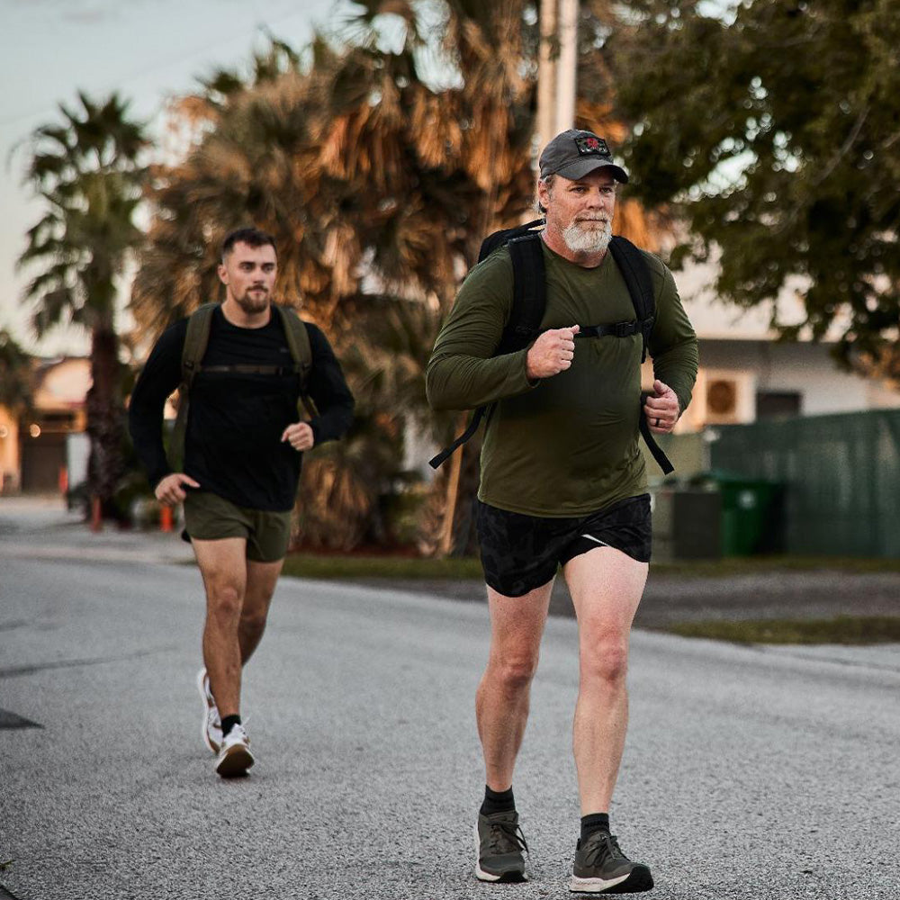 Two men wearing athletic clothing and backpacks jogging on a suburban street lined with palm trees.