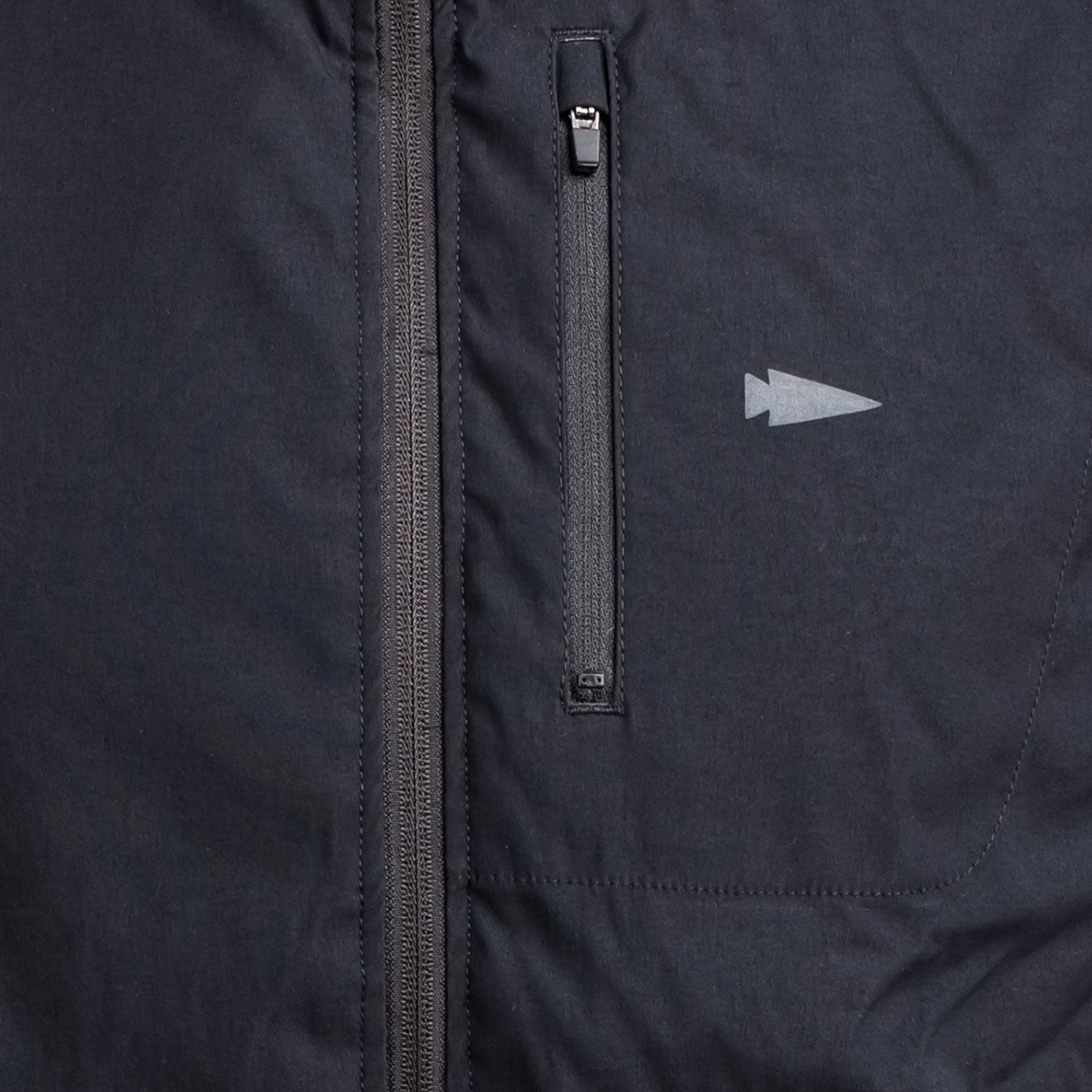 Close-up of a black jacket with a vertical zipper pocket and a small arrow logo on the chest.