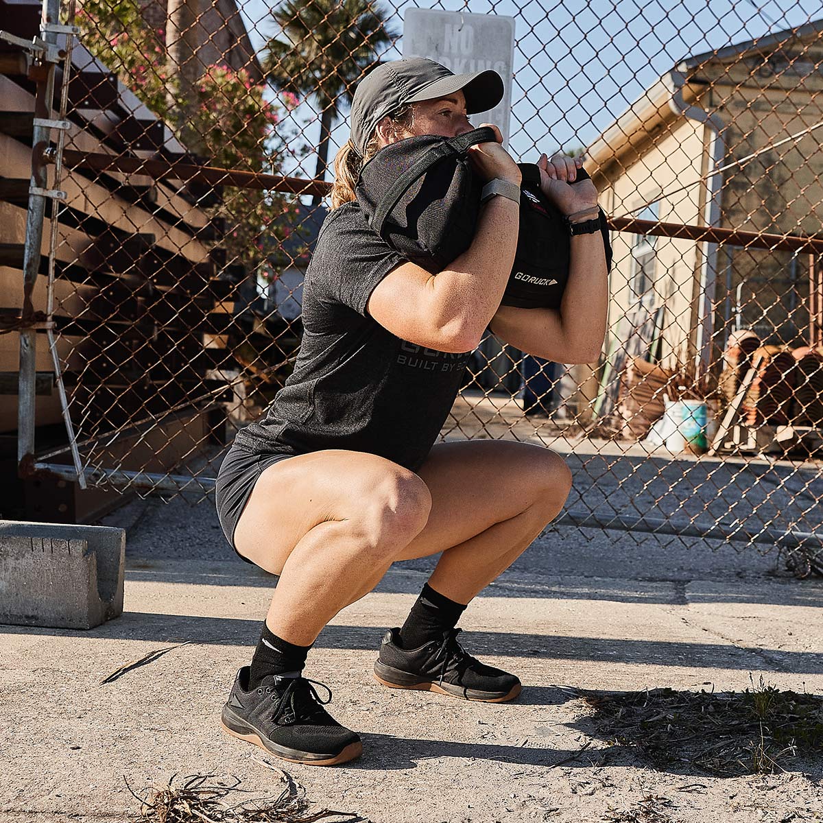 Athlete performing squat with GORUCK rucksack outdoors, wearing black GORUCK gear and shoes