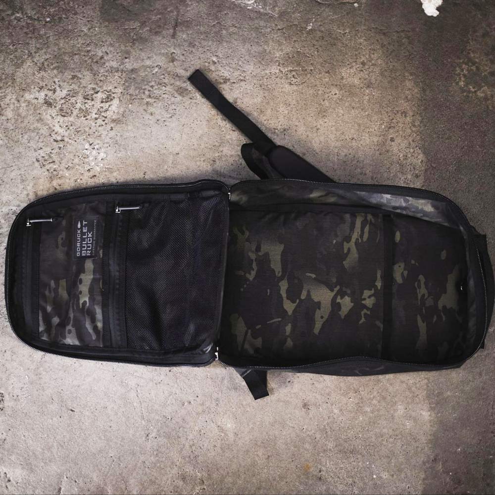 Open black camo backpack on concrete ground, showing mesh pocket and spacious main compartment.