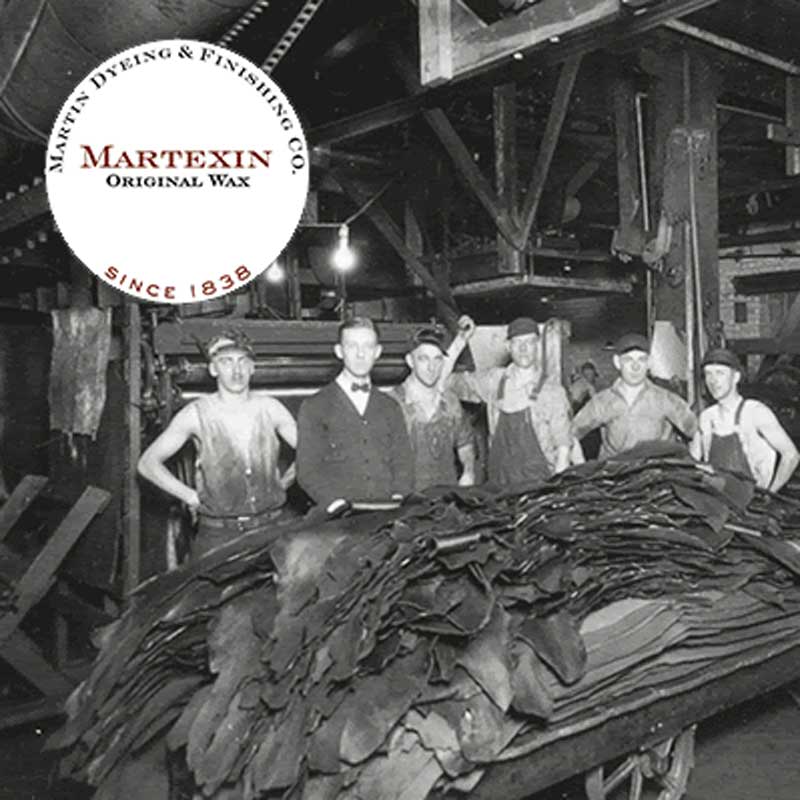 Black and white photo of factory workers posing by piles of fabric;