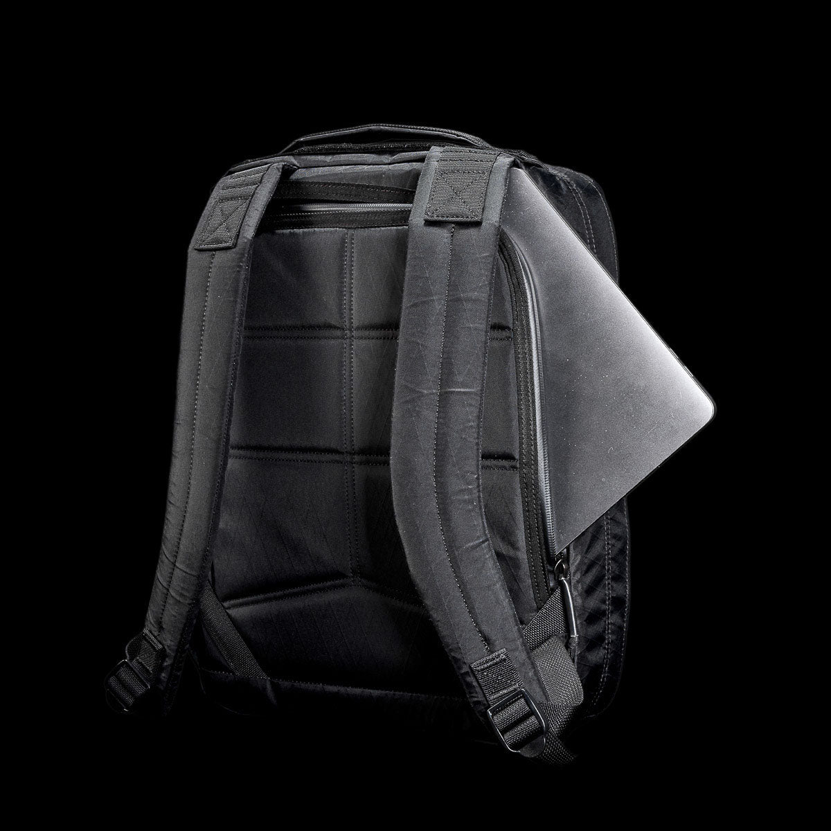 A black backpack with a laptop partially tucked into the back compartment, against a black background.