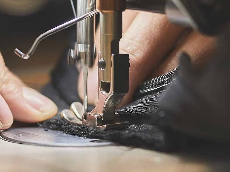 Close-up of a sewing machine needle stitching black fabric with a person's hand guiding the material.