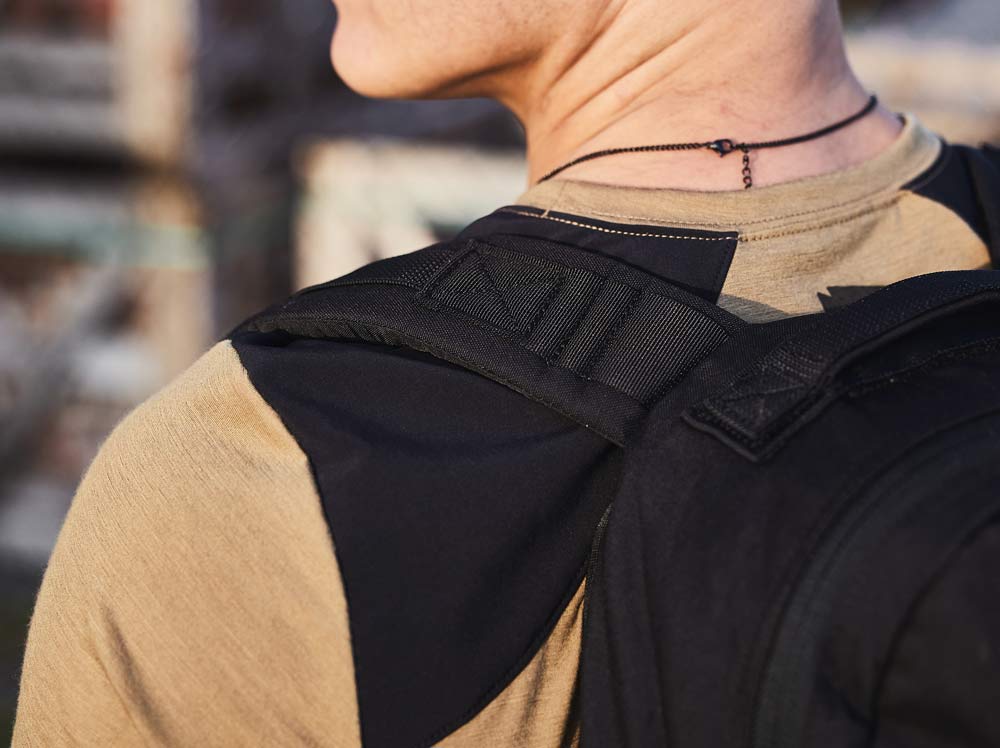 Close-up of a person wearing a tan shirt, black backpack, and a thin black necklace, seen from behind.