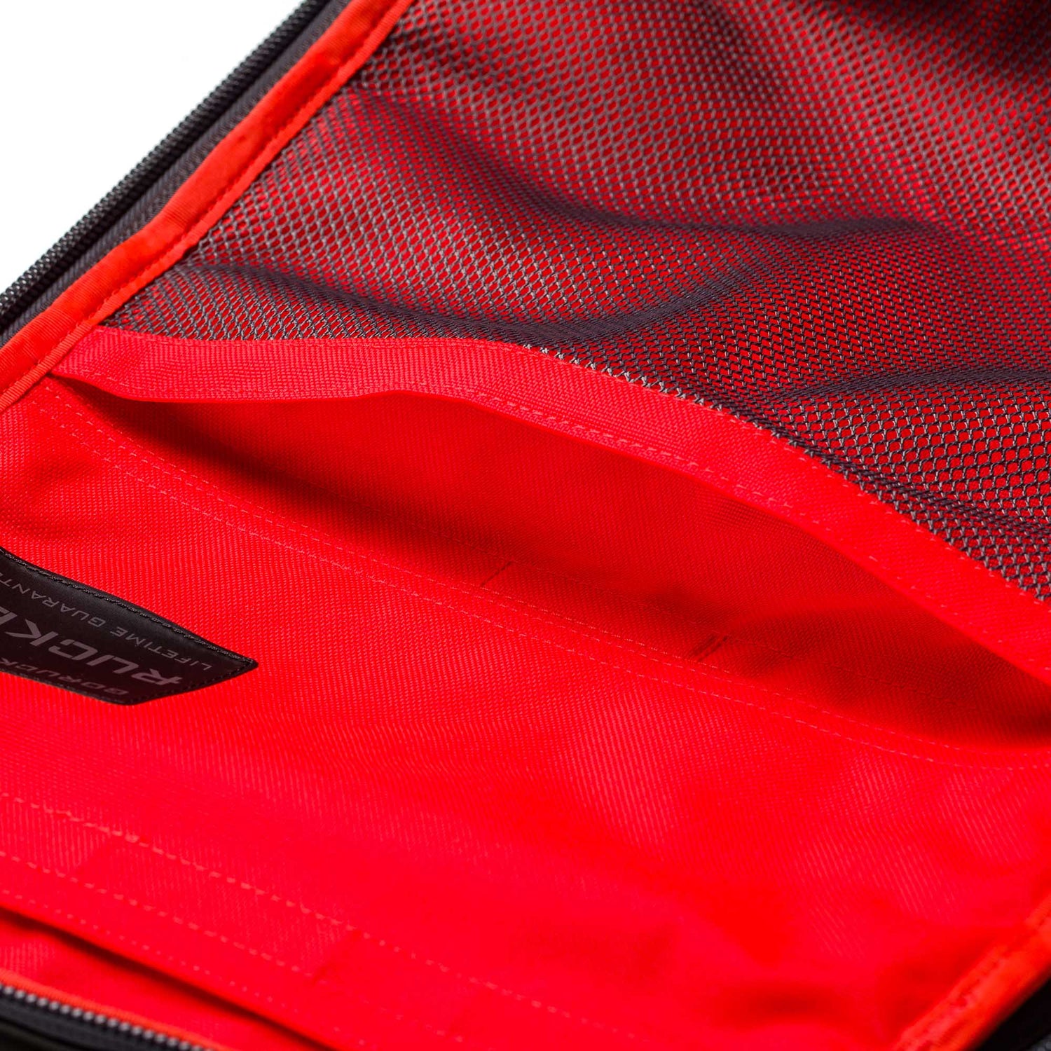 Close-up of an open Rucker 5.0 rucksack in red and black, featuring a zippered inner mesh pocket and a visible fabric label.