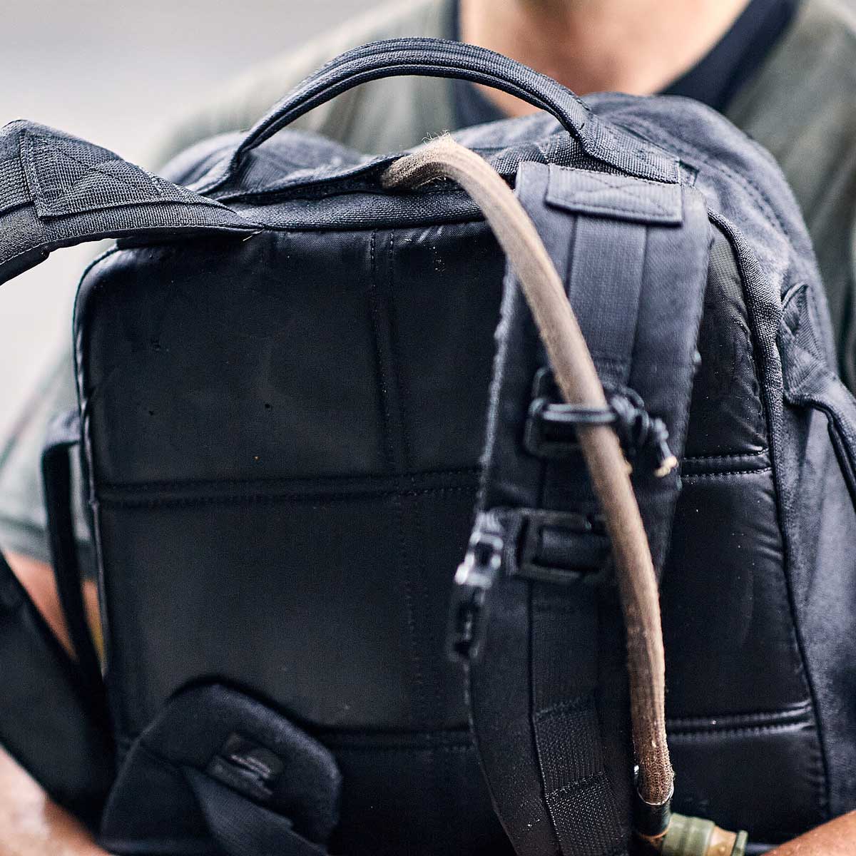Close-up of a person holding a black backpack with a hydration tube over the shoulder strap.