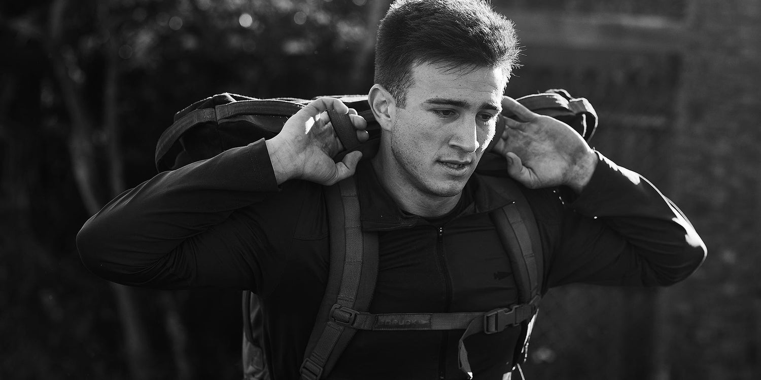 A man in a jacket carries a backpack on his shoulders, looking focused. Black and white photo.