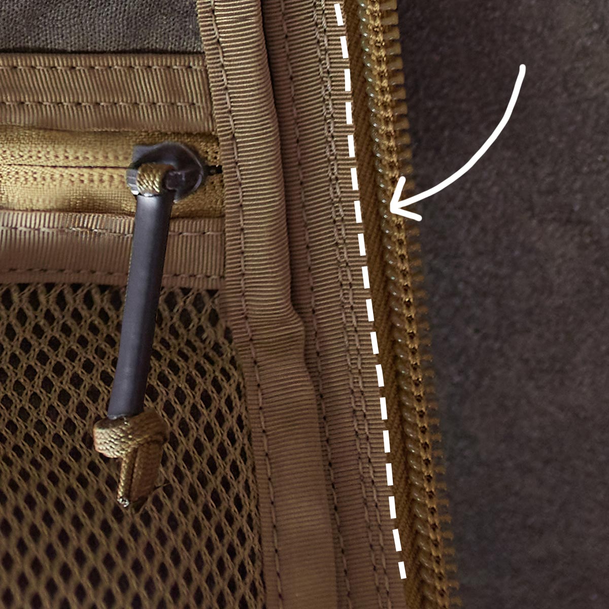 Close-up of a brown zipper with mesh pocket and black pull cord, highlighted by a white dashed line and arrow.