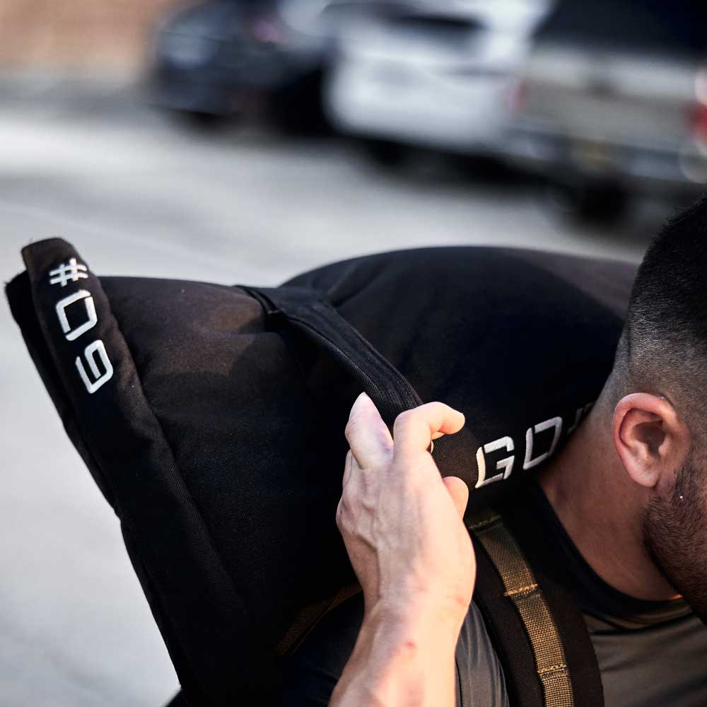 A person lifts a black sandbag marked