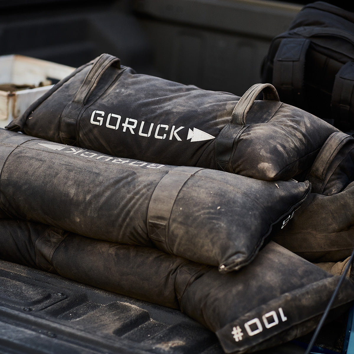 Three black GORUCK sandbags stacked in a truck bed, showing dust and wear.
