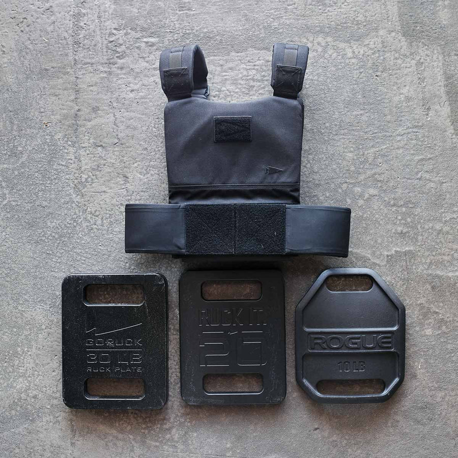 Black weighted vest and three metal weight plates (30 lb, 20 lb, 10 lb) on a concrete surface.