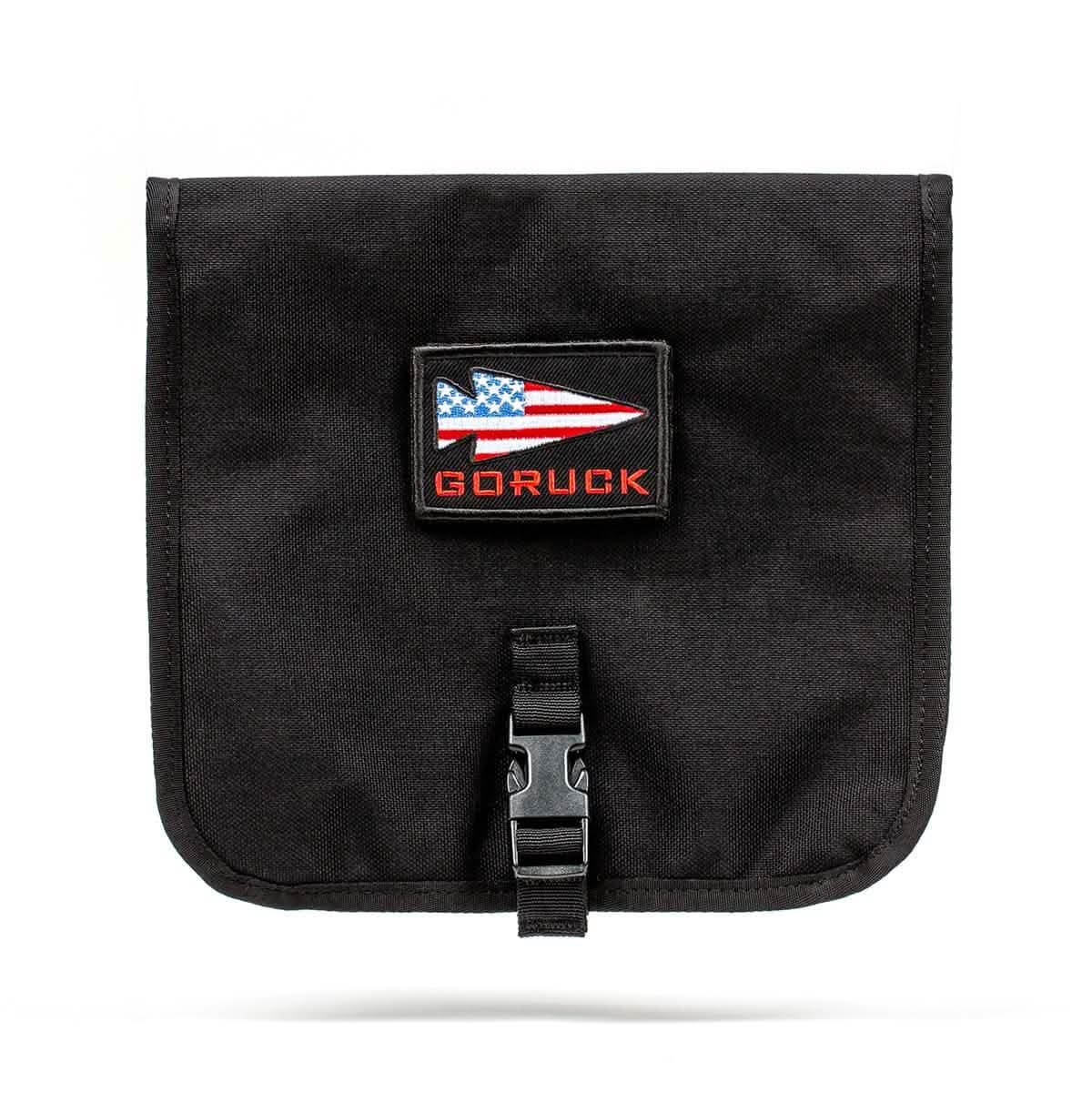 Introducing the GORUCK Wire Dopp: a black pouch designed for organized carry, featuring a flap adorned with a rectangular patch of an American flag and the brand name