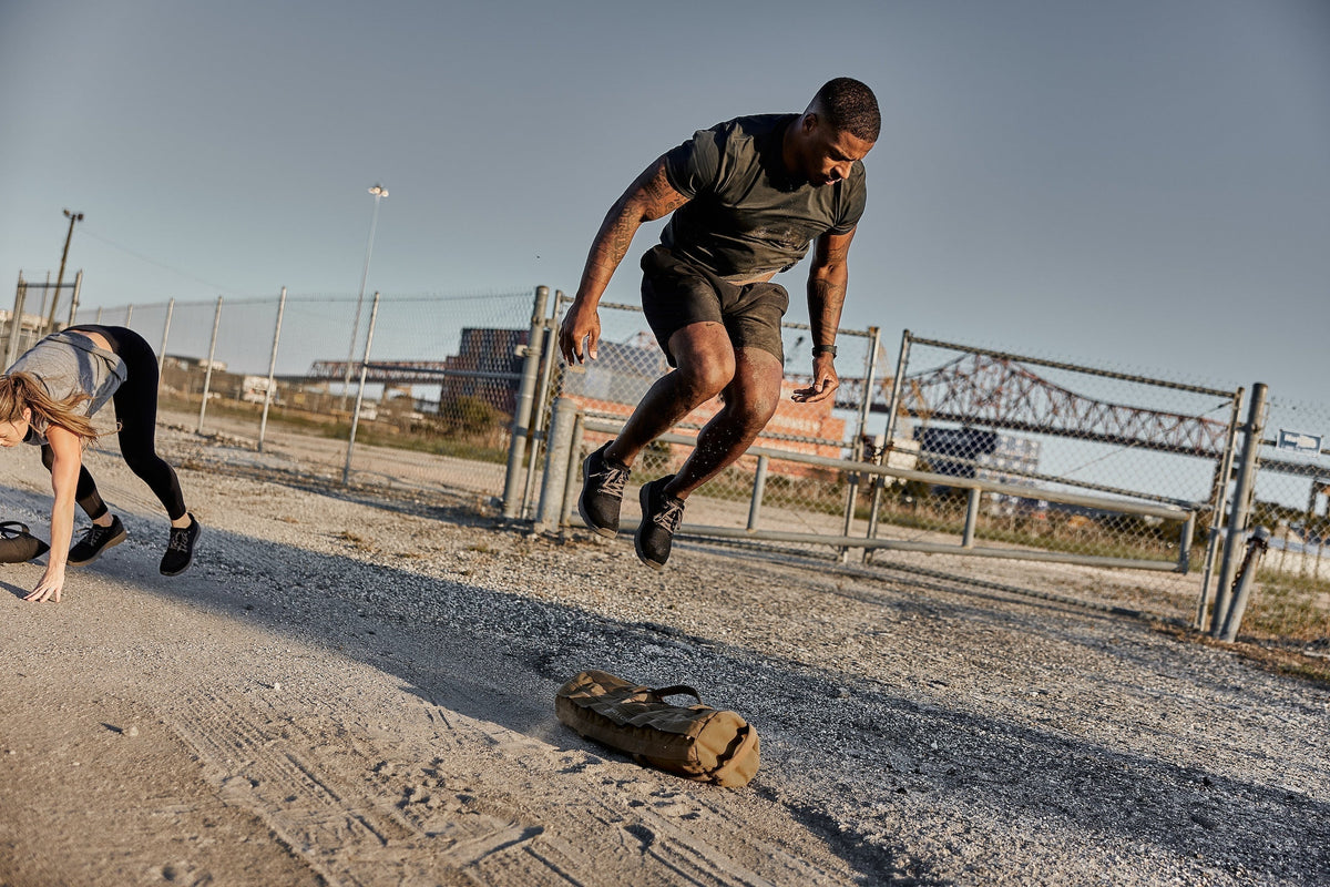 Man in athletic gear jumps over GORUCK sandbag outdoors during rucking fitness training