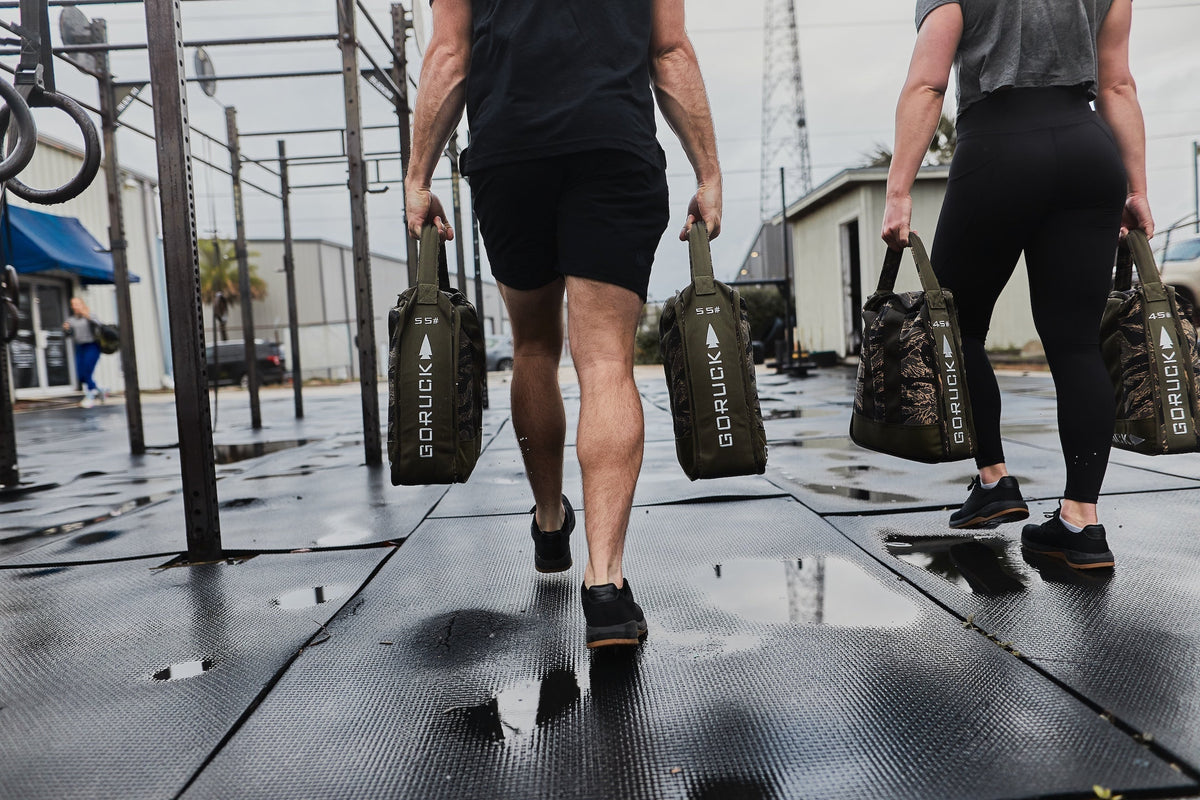 Two people rucking outdoors with GORUCK sandbags on a wet gym surface
