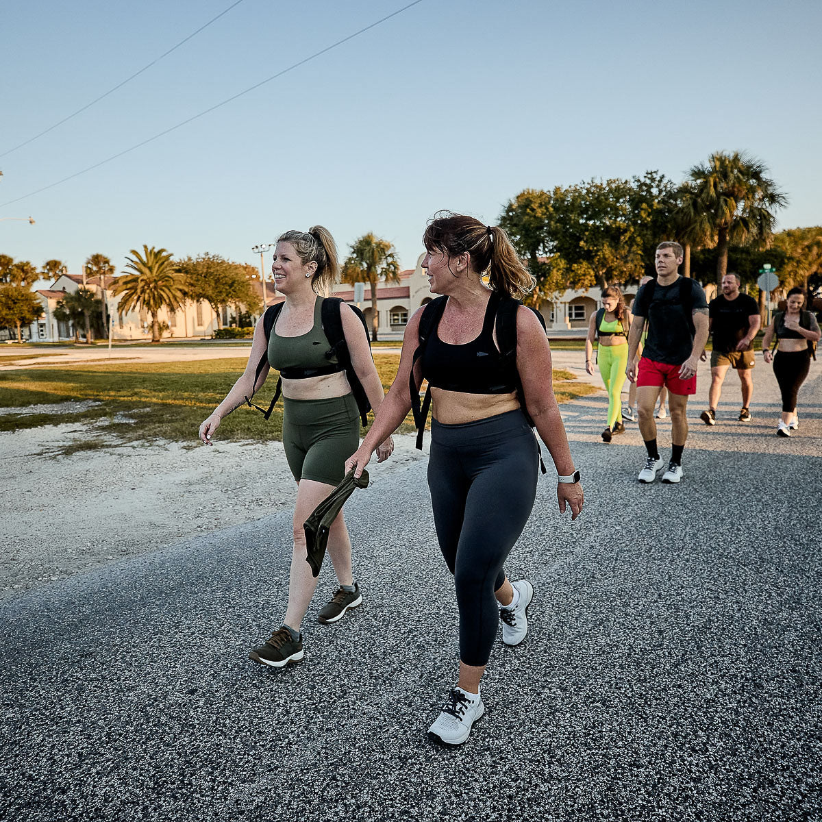 Group of people rucking outdoors in athletic gear, featuring GORUCK backpacks, on a sunny day