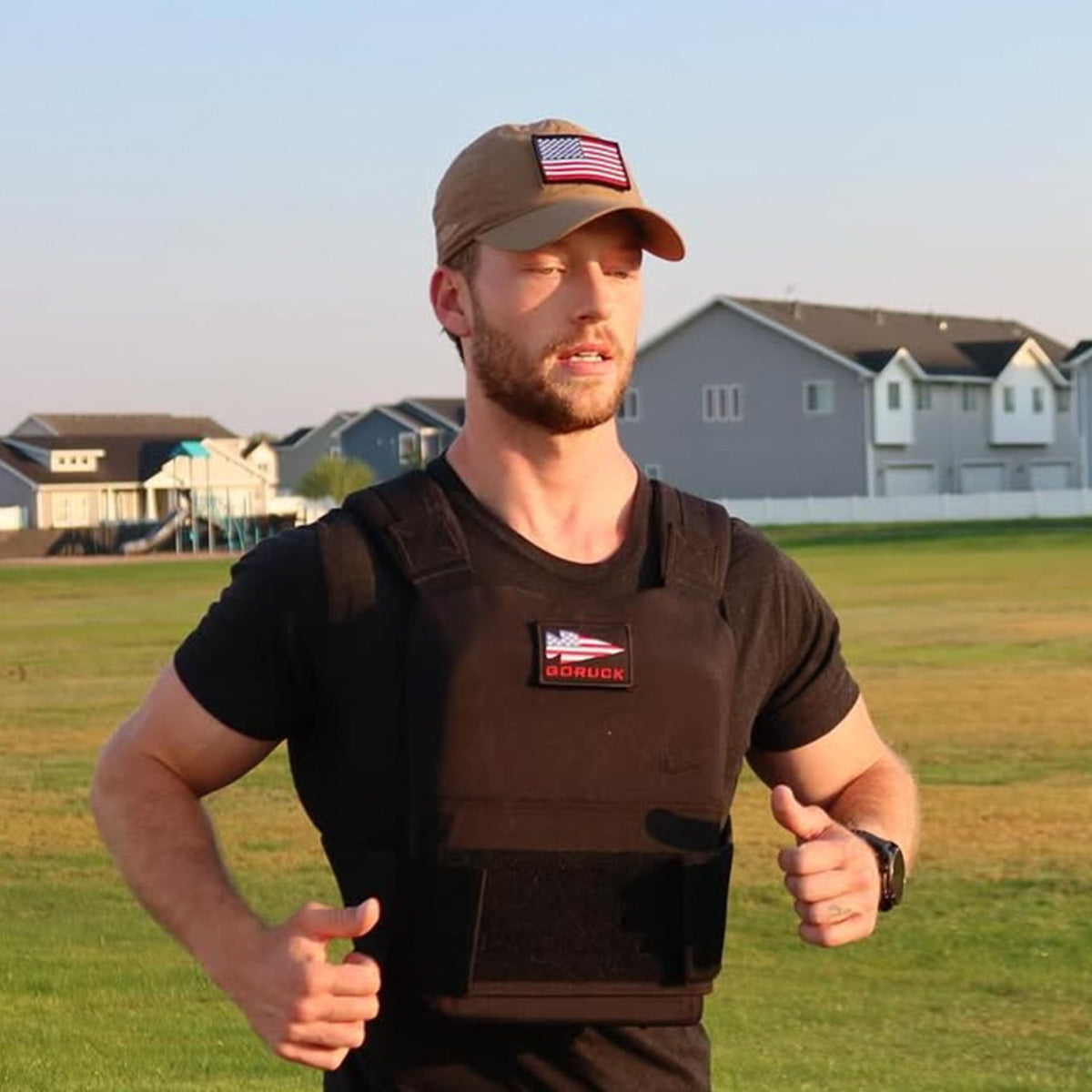 Man running outdoors wearing GORUCK training vest and cap, homes in background, rucking gear