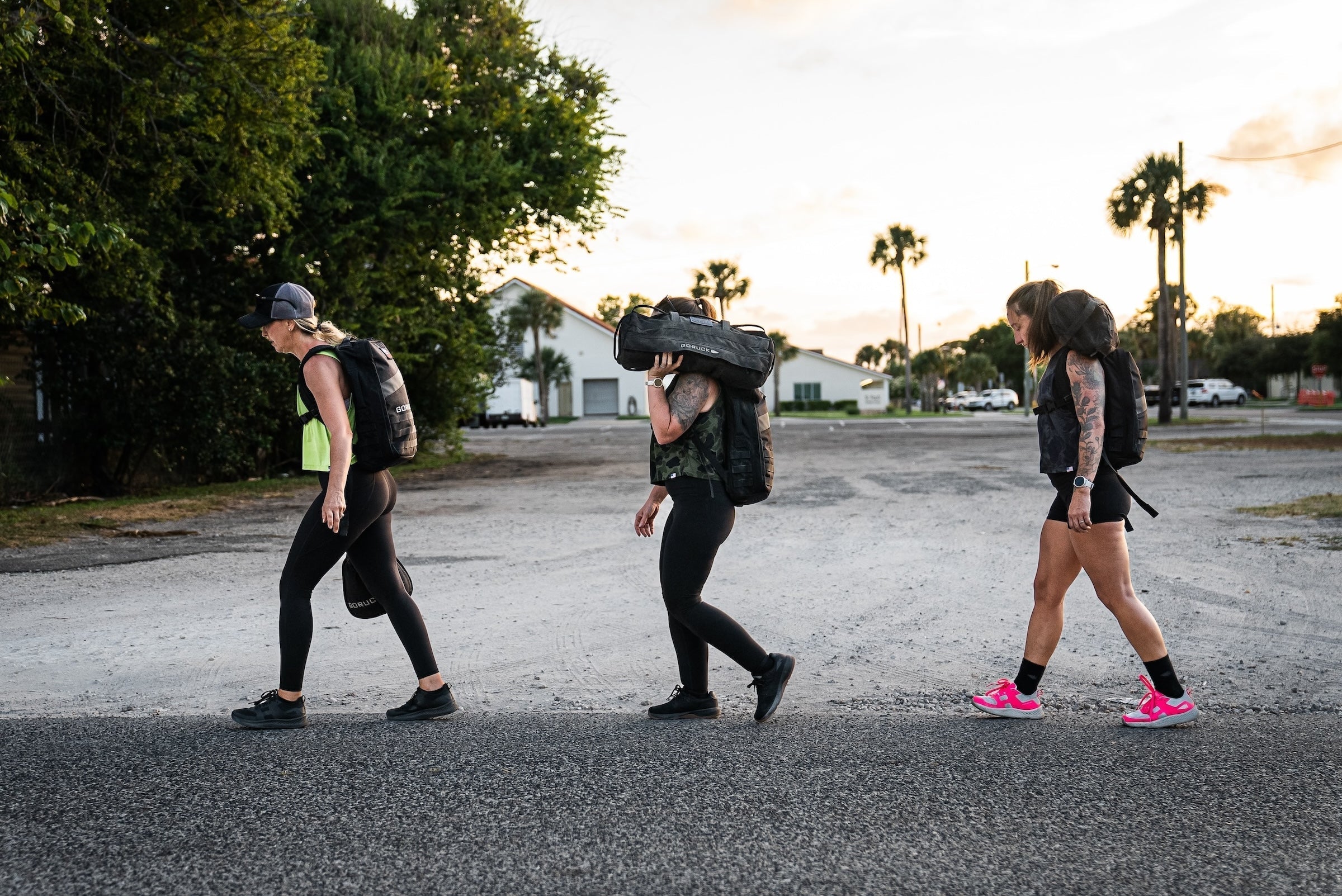 Three women rucking outdoors with GORUCK backpacks and gear at sunset