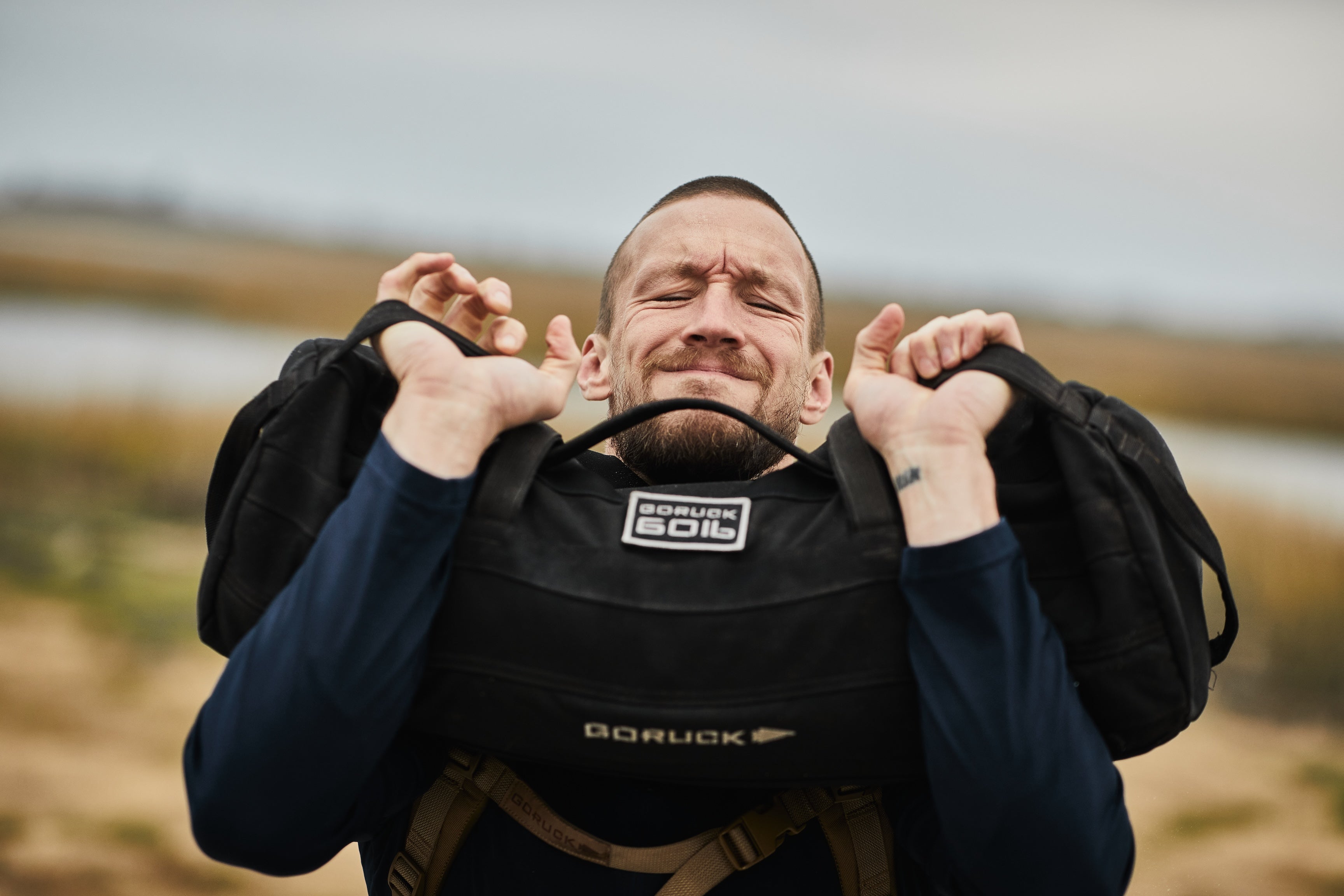 Man lifting GORUCK 60lb sandbag outdoors, showcasing tough rucking gear in action